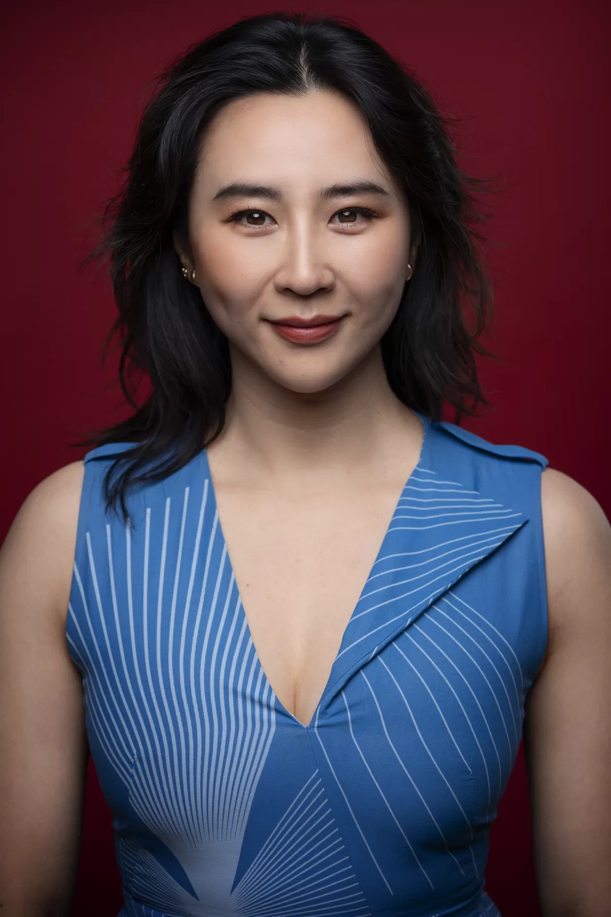 Commercial actor headshot of Erica Xia-Hou in a blue dress against a red background