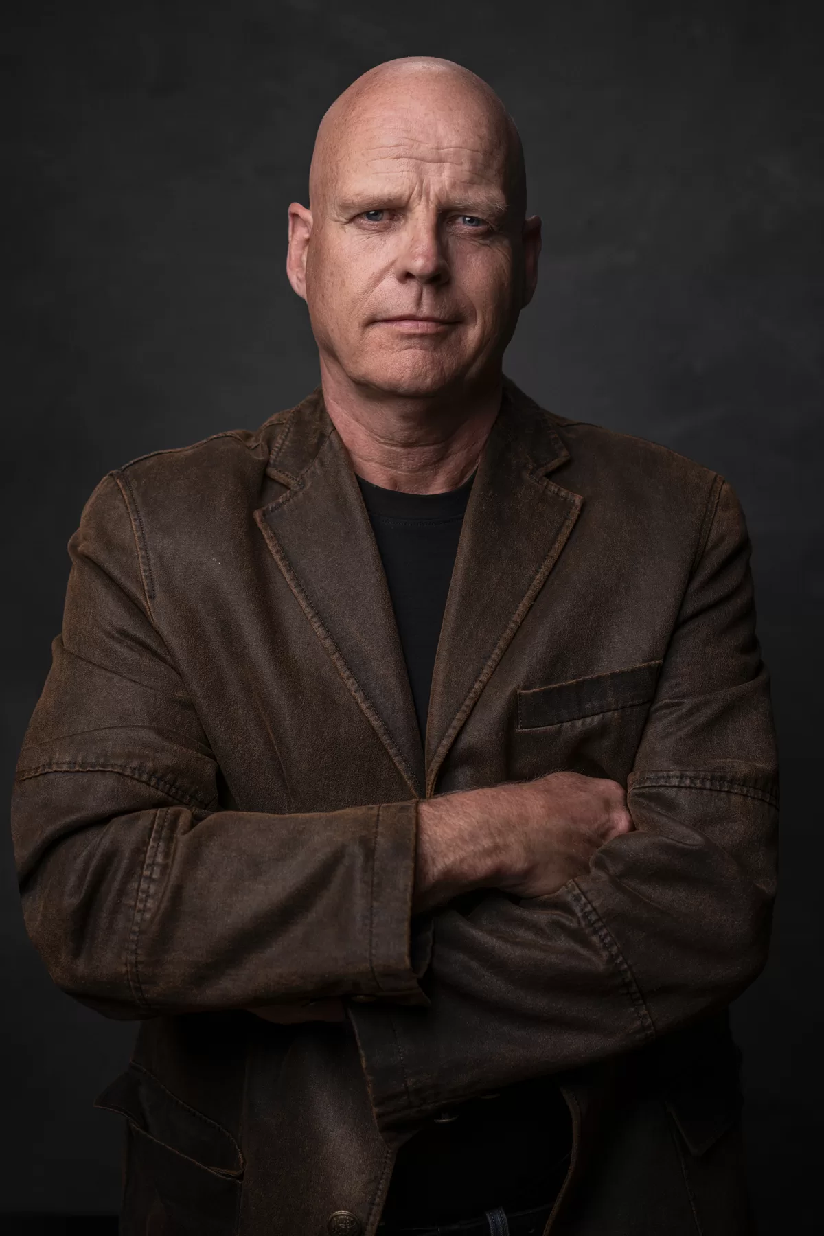 Theatrical portrait of Matt Evans in a brown jacket with arms crossed