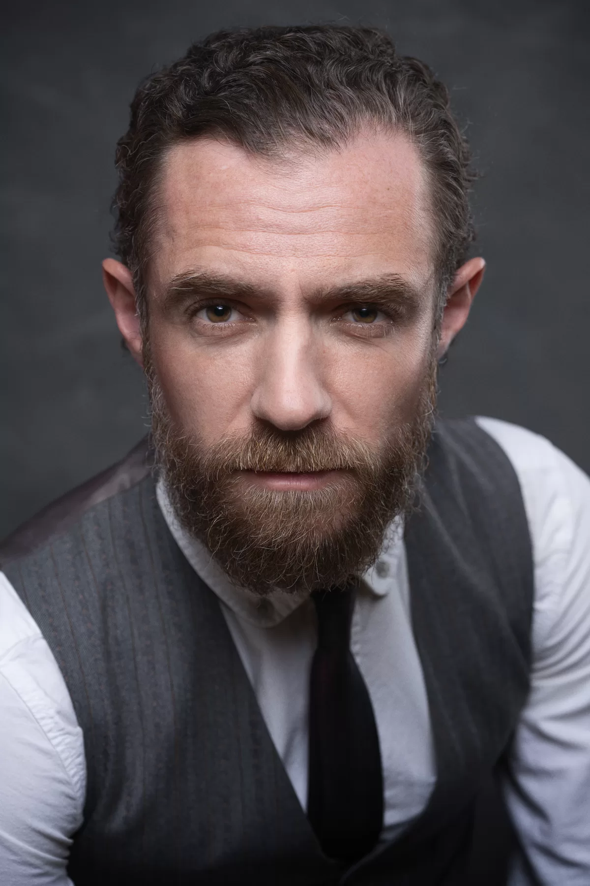 Intense Vancouver actor headshot of William with a beard and grey vest