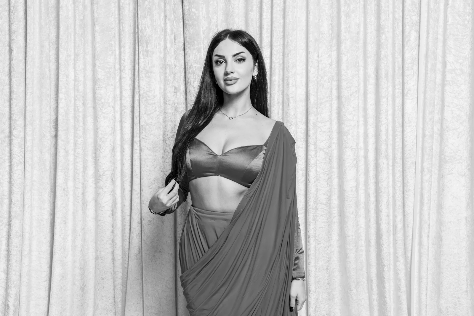 Guest posing in a flowing sari against the curtain backdrop