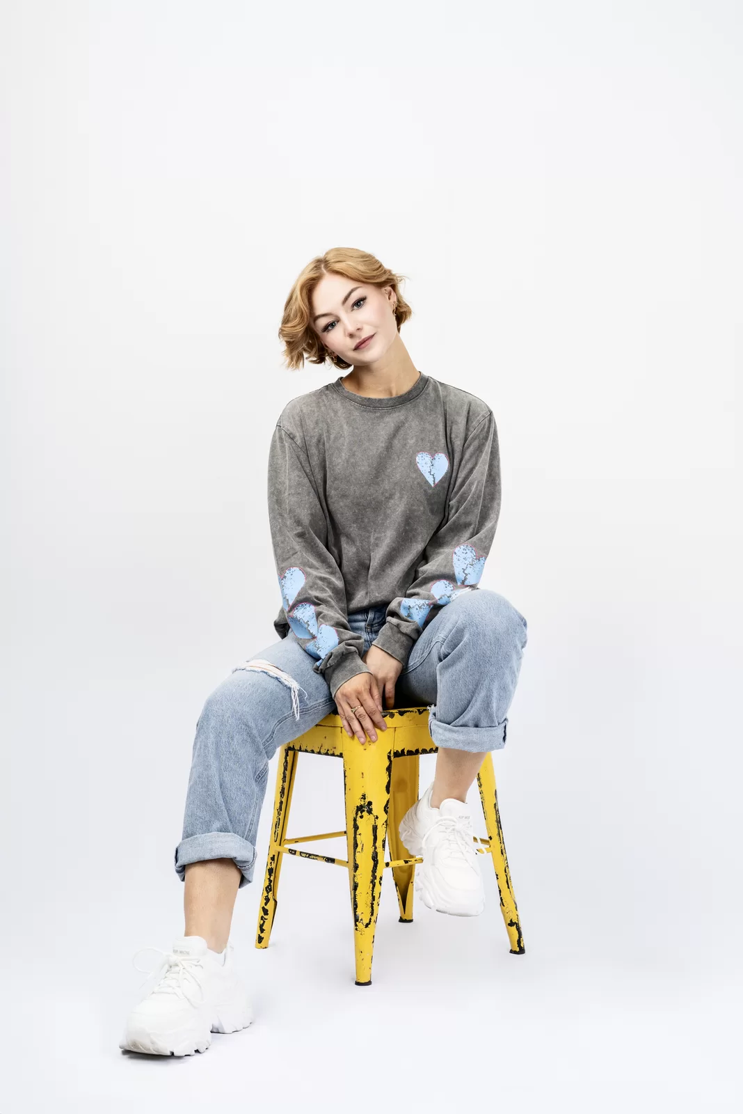 Studio branding portrait of Kall Me Kris seated on a yellow stool in a casual grey top